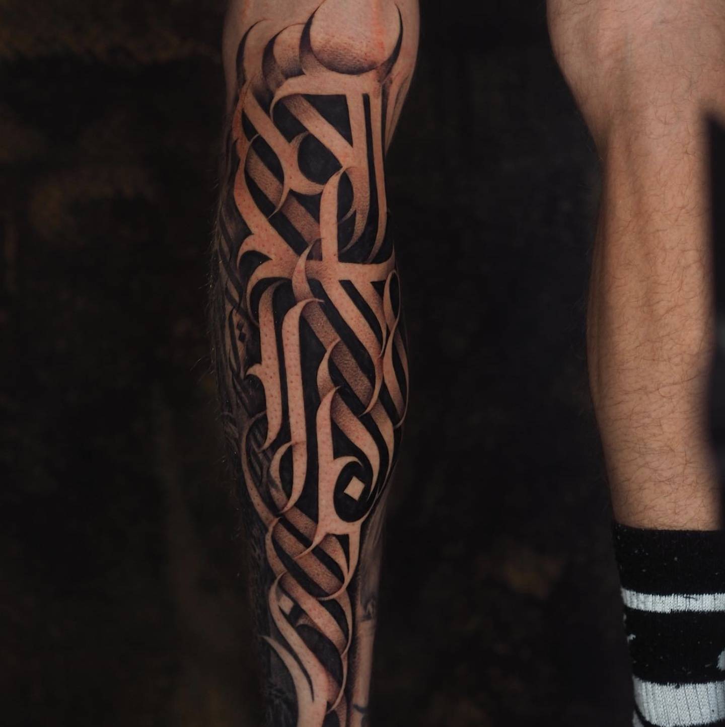 Upper arm tattoo featuring intricate black lettering with decorative elements and portrait elements